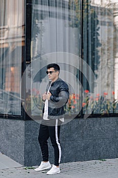 Young stylish guy in glasses in black leather jacket on glass background