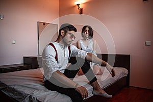 A young stylish guy in glasses and a young girl together sitting on the bed. the guy closer to the girl further. selective focus