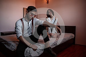 A young stylish guy in glasses and a young girl together sitting on the bed. the guy closer to the girl further. selective focus