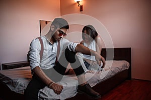 A young stylish guy in glasses and a young girl together sitting on the bed. the guy closer to the girl further. selective focus