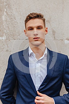 Young stylish guy with a monumental face walks in a cool city near the wooden and stone walls