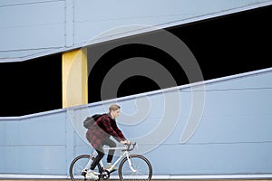 Young stylish guy rides a white bicycle forward on a background of blue wall