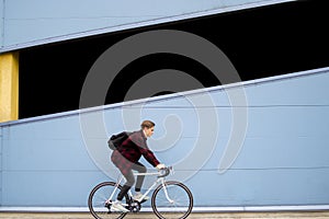 Young stylish guy rides a white bicycle forward on a background of blue wall