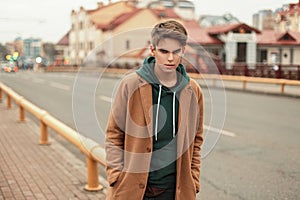 Young stylish guy in a trendy coat with a hoodie walks