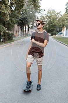 Young stylish handsome hipster man in fashionable summer clothes is riding on a snowboard. American cool modern guy