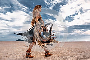 Young stylish hippie woman with big stylish bag walking on the beach at sunset