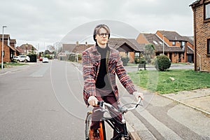 Young stylish hipster man riding on city Bicycle on the road of suburbs area among houses. Student on way to college on