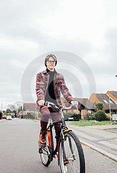 Young stylish hipster man riding on city Bicycle on the road of suburbs area among houses. Student on way to college on