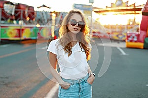 Young stylish hipster woman in trendy jeans in stylish sunglasses in trendy t-shirt is enjoying the summer bright sunshine