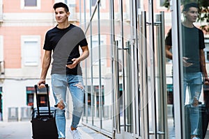 Young stylish man with black T-shirt and ripped jeans carrying a luggage