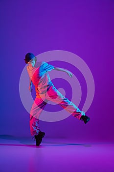 Young stylish man, break dancing, hip-hop dancer practicing solo in casual clothes isolated over purple background in