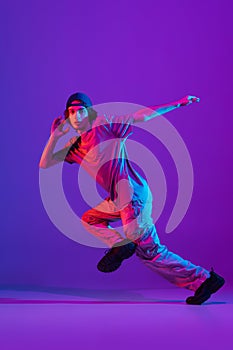 Young stylish man, break dancing, hip-hop dancer practicing solo in casual clothes isolated over purple background in