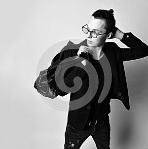 Young stylish man with a bun on head in glasses, black jeans, t-shirt and with a big stylish bag on his shoulder looks back