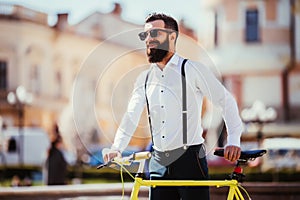 Young stylish man going to work by bike. hipster with a fixie bicycle on the street. bearded man looking away while riding on his