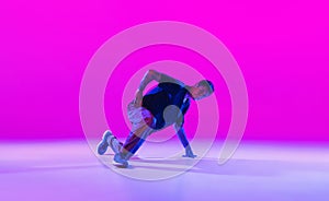 Young stylish man, hip-hop dancer dancing solo in modern clothes isolated over bright magenta background at dance hall