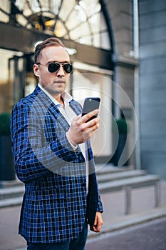 Young stylish man holding a mobile phone in the city center. Man wearing jacket and shirt