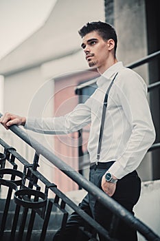 Young stylish man model in classic clothes posing near stairs. Fashion shot