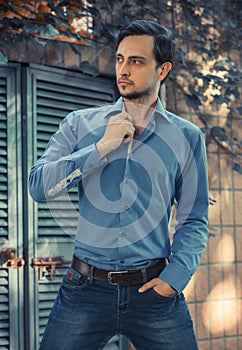 Young stylish man model in jeans and shirt posing in modern park architecture place. Fashion shot.