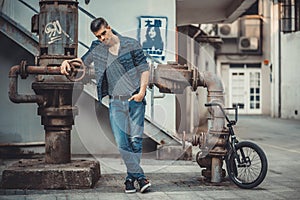 Young stylish man model near the loft metal tube and bike.