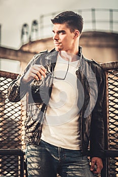 Young stylish man model posing in leather jacket and sunglasses.