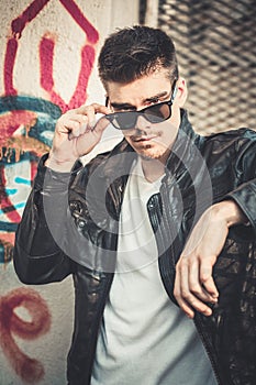 Young stylish man model posing in leather jacket and sunglasses.