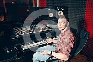 Young stylish man sitting on chair in front of monitor and soundboard