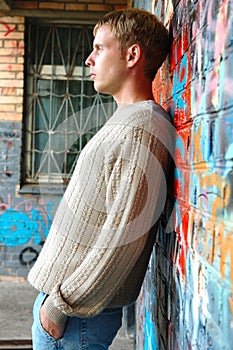 Young stylish man stand near graffiti brick wall.