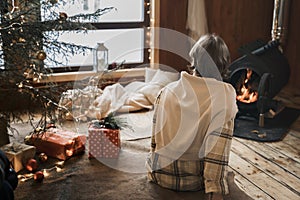 Young stylish man is stoking stove, reading cook. Celebrating new year eve in cozy wooden country house in winter forest