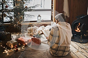 Young stylish man is stoking stove, reading cook. Celebrating new year eve in cozy wooden country house in winter forest