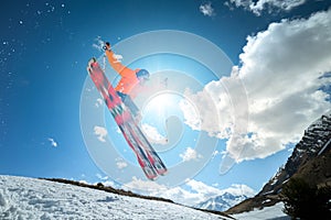 A young stylish man in sunglasses and a cap performs a trick in jumping with a kicker of snow against the blue sky and