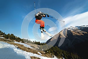 A young stylish man in sunglasses and a cap performs a trick in jumping with a kicker of snow against the blue sky and
