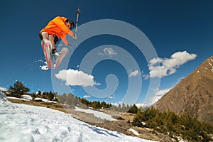 A young stylish man in sunglasses and a cap performs a trick in jumping with a kicker of snow against the blue sky and