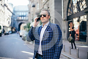 Young stylish man in sunglasses talking on a mobile phone in the city center. wearing a blue jacket and white shirt