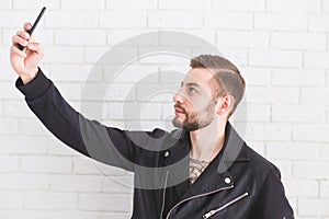 Young stylish man takes selfie on smartphone on white background.