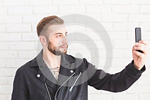 Young stylish man takes selfie on smartphone on white background.