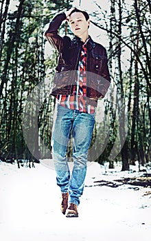 A young stylish man walking through snowy forest