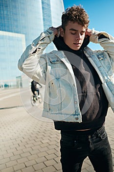 Young stylish man wearing denim jacket with hoodie during walk through street