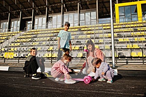 Young stylish mother with four kids outdoor. Sports family spend free time outdoors with scooters and skates. Painted with chalk