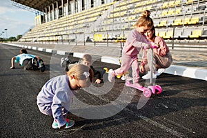 Young stylish mother with four kids outdoor. Sports family spend free time outdoors with scooters and skates. Painted with chalk