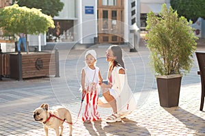 A young stylish mother with her daughter and her dog, a French bulldog, on a walk in the city.