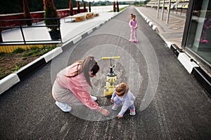 Young stylish mother with two girls outdoor. Sports family spend free time outdoors with scooters. Painted with chalk on the