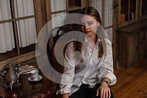 Young stylish pretty woman with trendy hairstyle in a fashionable white shirt in black jeans enjoys a rest on the chair in a