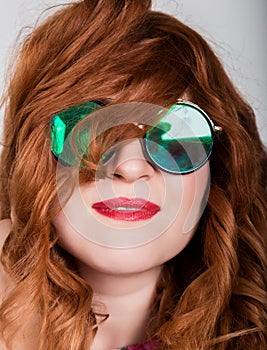 Young stylish red-haired woman with curly hair and pretty face posing in sunglasses. expresses different emotions