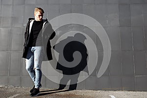 Young stylish redhead man in trendy outfit posing against urban background