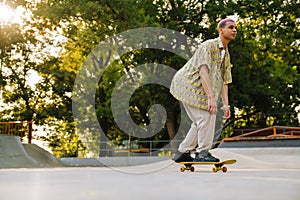 Young stylish short-haired boy riding skateboard in sunny skatepark