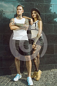 Young stylish tattooed couple standing at the tiled black wall on the street