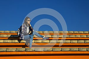 Young and stylish woman with camera sitting on the bech on sunny