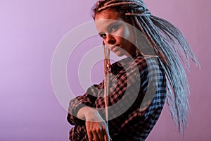 A young, stylish woman in dreadlocks poses in a neon light.