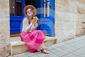 Young stylish woman eating fastfood on city street. Happy girl having pancake