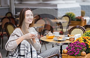 Young stylish woman having a french breakfast with coffee and cake sitting at the cafe terrace
